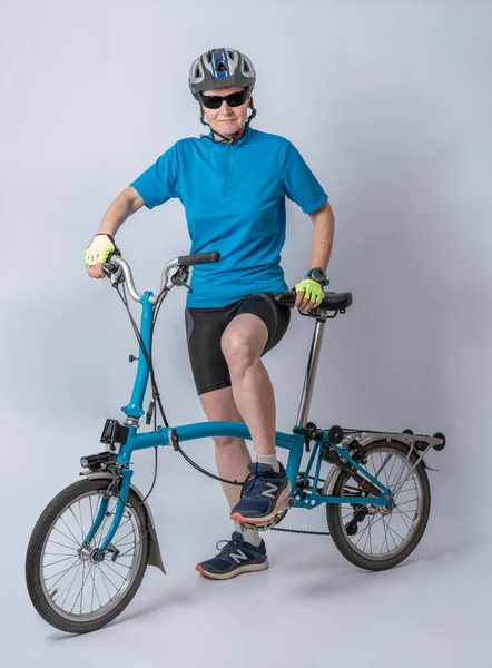 Studio shot detail of a woman dressed in a blue polo shirt, black shorts and a bicycle helmet, poses next to her blue folding bicycle