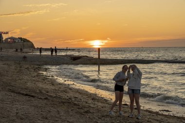 Langrune-Sur-Mer, Fransa - 07: 07 17 2023: Sahilin manzarası iki genç kızın gün batımında iskelede selfie çekmesi