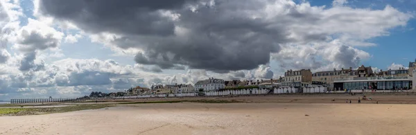 Luc-Sur-Mer, France, France - 07 26 2023:  View of a cloudy rainy sky, the wooden Fisherman\'s Pier, the seawall, beach cabins and people above the sea from the beach