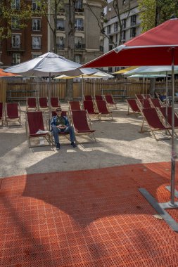 Paris, Fransa - 08: 27 2023: Paris Plajları. Bassin de la Villette rıhtımlarında beyaz bir şemsiyenin altında, güverte sandalyesinde oturan olgun bir kadın.