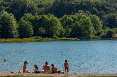 Virieu Gölü, Fransa - 08 31 2021: Grand Colombier Geçidi. Göletin kenarında oturan üç çocuklu bir çiftin görüntüsü