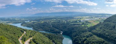 Ovanın üst kalesinden seralar, Rhone nehri, Vuache dağı bir köprü, bir yol ve bir tren yolu görünüyor.