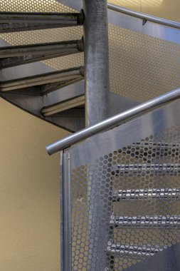 Dairesel metal bir merdiven ve arkasında sarı bir cephe.