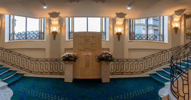 Dairesel mermer bir merdiven manzarası mavi ve yeşil bir halı ve demir merdiven önü görünüyor.