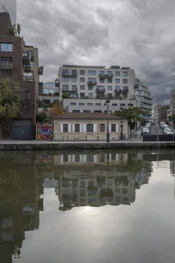 Paris, Fransa - 11 26 2023: Ourcq Kanalı. Eski bir taş evin Ourcq kanalı ve arkadaki modern bir binanın yansımaları.