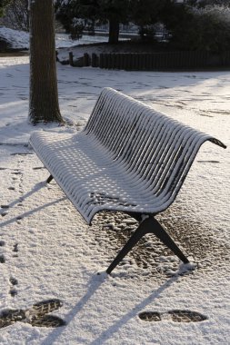 Eko-mahalle. Ağaçların manzarası ve parktaki karla kaplı metal bir bank.