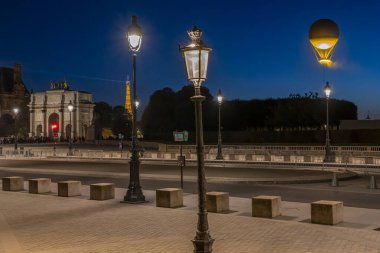 Paris, France - 08 05 2024: Olympic Games Paris 2024. View of the Olympic cauldron behind Arc de Triomphe of Carrousel du Louvre and Napoleon courtyard of Louvre Museum by night clipart