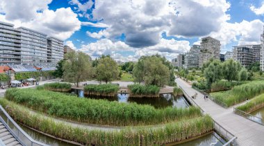 Paris, France - 07 20 2024: Clichy-Batignolles Martin Luther King Park. view of the park's pond reeds, vegetation, railroad and the buildings around clipart