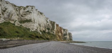 Kayalıkların manzarası, iskele, çakıl taşı plajı, mavi deniz ve bulutlu bir gökyüzü.