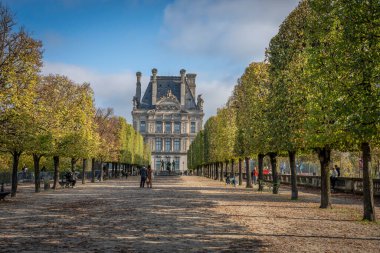 Paris, Fransa - 11 01 2024: Tuileries bahçesi. Kesilmiş ağaçlar, bronz heykeller ve Le Louvre cephesiyle kaplı geniş bir patika manzarası