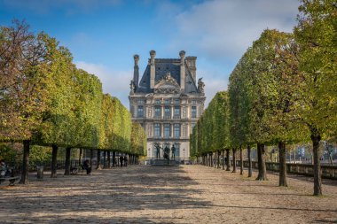 Paris, Fransa - 11 01 2024: Tuileries bahçesi. Kesilmiş ağaçlar, bronz heykeller ve Le Louvre cephesiyle kaplı geniş bir patika manzarası
