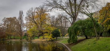 Paris, Fransa - 116 2024: Park Buttes Chaumont. Parkın orta kısmını yaya köprüsü, Belvedere adası, Sibyl Tapınağı, göl, fevkalade ağaçlar ve sonbahar renkleriyle bitki örtüsü ile görün.