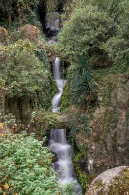 Paris, Fransa - 116 2024: Park Buttes Chaumont. Sonbahar renkleriyle suni şelale ve bitki örtüsü manzarası