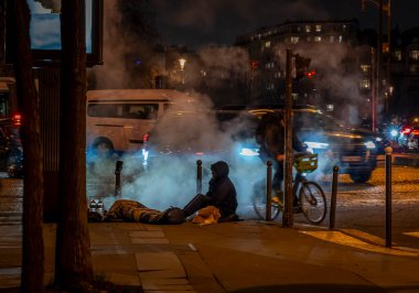 Paris, Fransa - 12: 2024: Evsiz bir adam Paris caddesinde gece sigara içen bir havalandırmada oturuyor