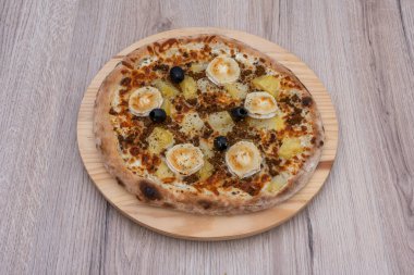 İtalyan mutfağı natürmort. Patatesli, sucuklu, zeytinli ve peynirli bir çiftlik pizzası. Yukarıdan görülüyor ve ahşap bir tepsiye konuyor.