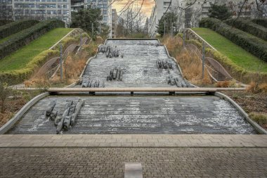 Courbevoie, France - 04 16 2020: Diderot Park. View of the Defense towers district, garden and waterfall at sunset in winter clipart