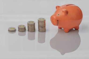 Yakın plan, dört deste iki euro bozukluk ve ahşap bir masaya yansıyan pembe domuz kumbarası.
