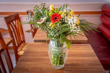 Ahşap bir masanın üzerine konmuş şeffaf bir vazoda karışık çiçeklerden oluşan bir buket.