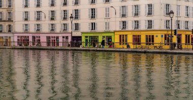 Paris, Fransa - 02 23 2022: Canal Saint-Martin. Beyaz ve kıvrımlı binaların panoramik manzarası ve suya yansıyan renkli depoların