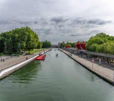 Paris, Fransa - 07 07 07 2024: La Villette Parkı. Flander Köprüsü 'nden havza kanalı manzarası. Tekneler, park, gökyüzü, köprü, binalar ve Pantin' in Les Grands Moulins 'i.