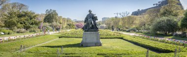 Paris, Fransa - 04 05 2025: Jardin des Plantes. Botanik bahçesinin panoramik manzarası Jean Carlus 'un heykeli ve arkasında iki büyük Japon kiraz ağacı.