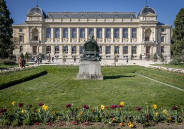 Paris, Fransa - 04 05 2025: Jardin des Plantes. Botanik bahçesinin panoramik manzarası, Jean Carlus 'un heykeli ve arkasındaki Büyük Evrim Galerisi.