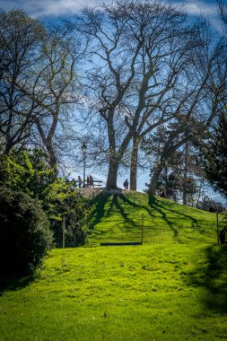 Paris, Fransa - 04 06 2025: Buttes-Chaumont Parkı. Tepe ışıklarında yaprakları olmayan devasa ağaçların panoramik manzarası