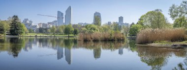 Nanterre, Fransa - 04 11 2025: Andre Malraux Parkı. Gölün panoramik manzarası, yapraktaki ağaçlar, sazlıklar ve arka tarafta yansıyan La Defense kuleleri.