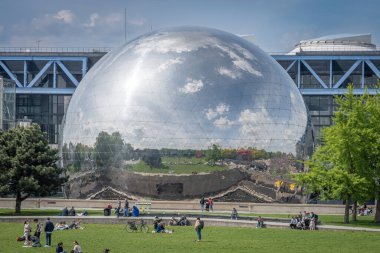 Paris, Fransa - 04 26 2025 Villette Kanalı. La Geode 'nin panoramik manzarası parkın yansıması, çimlerin üzerindeki insanlar ve arkadaki Bilim ve Sanayi Müzesi binası