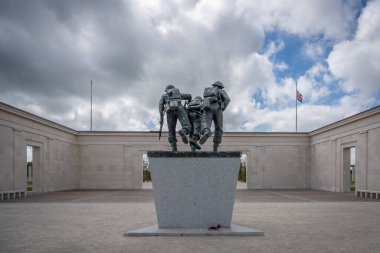 Vers-Sur-Mer, Fransa - 05 16 2025: British Normandy Memorial. Üç silahlı İngiliz askeri, arkasında bayraklar ve anıt bulunan bir heykel üzerinde dikiliyor ve koşuyorlar.