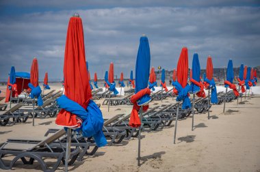 Deauville, Fransa - 05: 17 2025 Deauville Plajı. Sahilin panoramik manzarası renkli şemsiyeler, şezlonglar, deniz ve bulutlu mavi gökyüzü