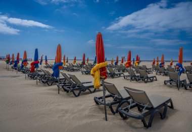 Deauville, Fransa - 05: 17 2025 Deauville Plajı. Sahilin panoramik manzarası renkli şemsiyeler, şezlonglar, deniz ve bulutlu mavi gökyüzü