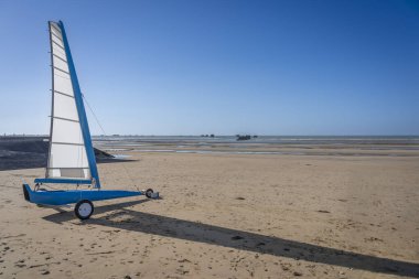 Asnelles-Sur-Mer, Fransa - 05: 16 2025: Kum ve deniz arasında sahil boyunca bir yelkenli tarafından itilen beyaz ve mavi bir kara yatı manzarası