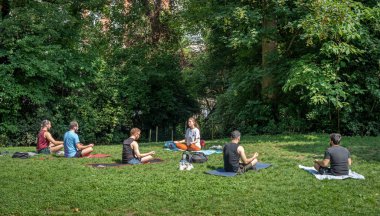 Paris, Fransa - 06 14 2025: Buttes-Chaumont Parkı. Çimlerin üzerinde oturup yoga ve bitki örtüsü yapan bir grup insanın görüntüsü.