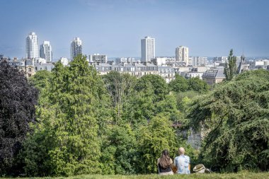 Paris, Fransa - 06 14 2025: Çimlerin üzerinde oturan ve parka ve Ourcq ilçe binalarına bakan bir çiftin panoramik manzarası