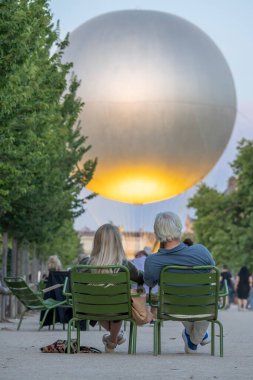 Paris, Fransa - 07 03 2025: Koltuklarda oturan yaşlı bir kadın ve erkek, önlerindeki Tuileries bahçesinde Olimpiyat kazanına bakıyorlar