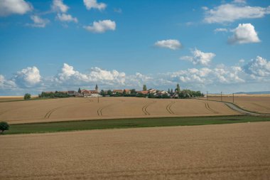 Reims, Fransa - 06 26 2025: Ekili tarlaların panoramik manzarası, demiryolu hattı boyunca tipik bir köy ve bulutlu gökyüzü