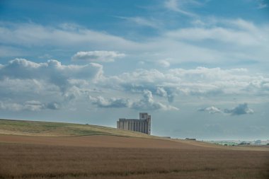 Reims, Fransa - 06 26 2025: Tarım alanlarının panoramik görünümü, dikey, silindirik beton buğday silosu, demiryolu hattı boyunca bulutlu gökyüzü ile dolu