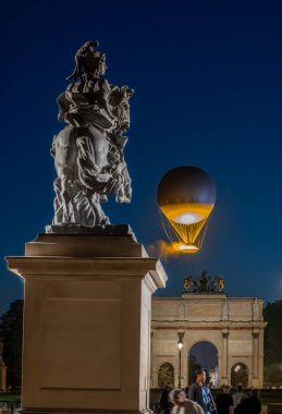 Paris, Fransa - 07 28 2025: Akşam üzeri Louis XIV ve Le Carrousel du Louvre heykelinin arkasında uçan Olimpiyat Kazanı 'na bakın.