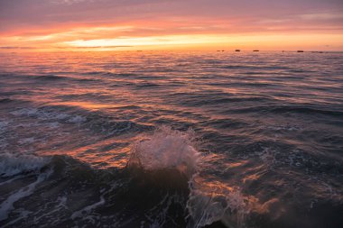 Denizin panoramik manzarası, dalgalar ve iskele boyunca gün batımında renkli bulutlu gökyüzü.