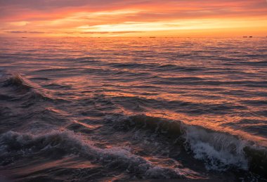 Denizin panoramik manzarası, dalgalar ve iskele boyunca gün batımında renkli bulutlu gökyüzü.