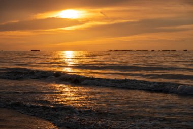 Denizin panoramik manzarası, dalgalar, yapay liman ve iskele boyunca gün batımında renkli bulutlu gökyüzü.