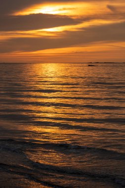 Denizin panoramik manzarası, dalgalar, yapay liman ve iskele boyunca gün batımında renkli bulutlu gökyüzü.