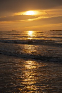 Denizin panoramik manzarası, dalgalar, yapay liman ve iskele boyunca gün batımında renkli bulutlu gökyüzü.