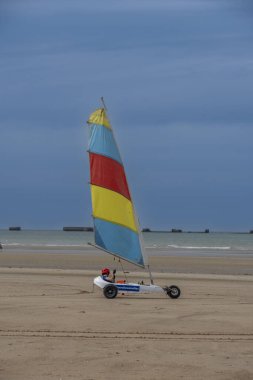 Asnelles-Sur-Mer, Fransa - 08 08 08 2025: Sahil boyunca deniz ve yapay liman ile kumsalda yarışan bir kara yatının görüntüsü