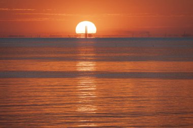Güneşin denizin üzerinde doğuşunun panoramik görüntüsü. Renkli ışığın yansımaları, güneş ve Le Havre uzaklarda.