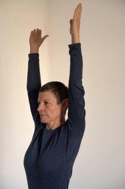 Mavi tişört ve mavi şort giyen olgun bir kadın evde yoga seansı yapıyor.