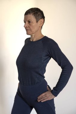 Mavi tişört ve mavi şort giyen olgun bir kadın evde yoga seansı yapıyor.