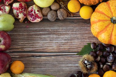 Taze sonbahar meyvesi (balkabağı, kestane, elma, mısır, nar, armut, ceviz) fotokopi alanı olan ahşap bir arka planda. Üst masa manzaralı. Sonbahar mevsiminde taze yiyecek çeşitliliği.