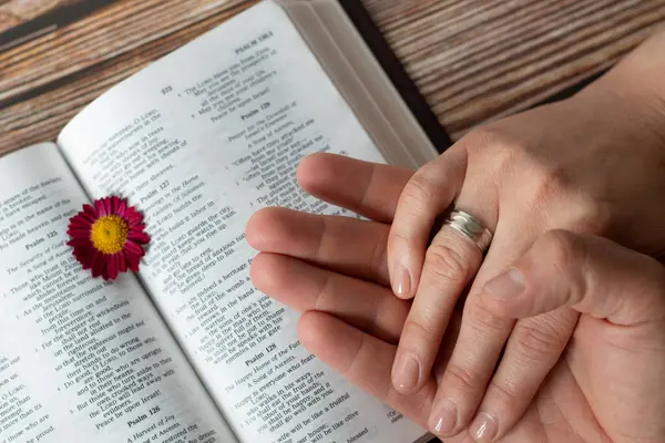 Christian couple hands with rings holding in prayer over open Holy Bible Book placedon wooden background. Top view. Christian marriage relationship, love, commitment, faithfulness, biblical concept.